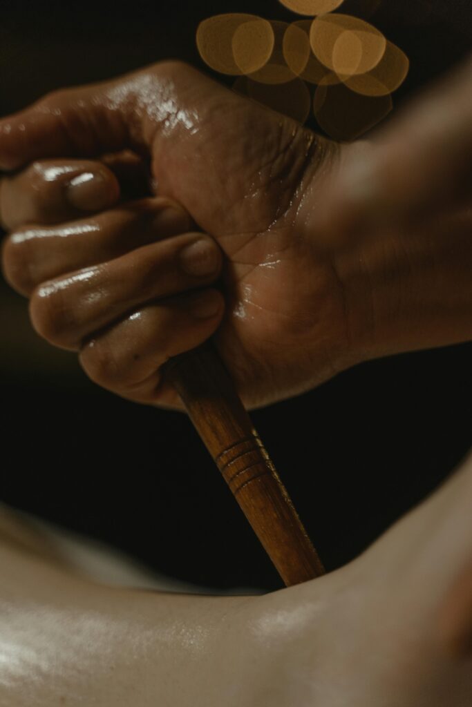pexels-photo-6187847-6187847 A close-up of a hand holding a wooden massage tool, set against a dark background.